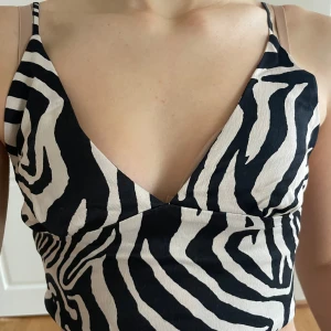 Zebramönstrad croppad topp - Snygg zebramönstrad croppad topp med djup v-ringning och smala axelband. Perfekt för en trendig look.
