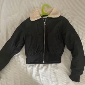 Svart bomberjacka från H&M med teddykrage - Säljer en svart bomberjacka från H&M med en mysig teddykrage i beige. Jackan har dragkedja framtill och långa ärmar. Perfekt för kyligare dagar och ger en cool look. 🖤