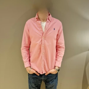 Rosa skjorta från Ralph Lauren - Snygg rosa skjorta från Ralph Lauren med klassisk krage och knappar framtill. Skjortan har långa ärmar och en liten broderad logga på bröstet. Perfekt för en stilren look. Tröjan passar XS/ S