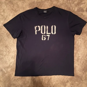Unik Ralph lauren t-shirt - Säljer en mörkblå t-shirt från Polo Ralph lauren Sport med trycket 'POLO 67' på framsidan. T-shirten är kortärmad och tillverkad i bomull, perfekt för en avslappnad stil.