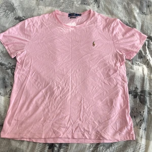 Rosa t-shirt från Ralph Lauren - Säljer en snygg rosa t-shirt från Ralph Lauren med en broderad logga på bröstet. Perfekt för en avslappnad stil. T-shirten har en klassisk passform och korta ärmar. Strynklig men ordnar sig om att stryka det. 