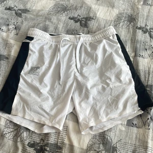Vita sportshorts med svarta detaljer - Snygga vita sportshorts med svarta paneler på sidorna och snörning i midjan. Perfekta för träning eller en aktiv dag. Lätta och bekväma med en modern look.