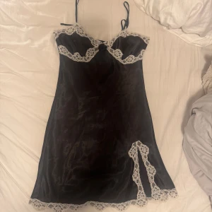 Nattlinne - Elegant svart nattlinne i siden med vackra vita spetsdetaljer längs kanterna och en liten rosett framtill. Klänningen har smala axelband och en feminin passform som ger en lyxig känsla. Storlek 36/38 vilket motsvarar S! Köp direkt för 199kr via köp nu💞💞
