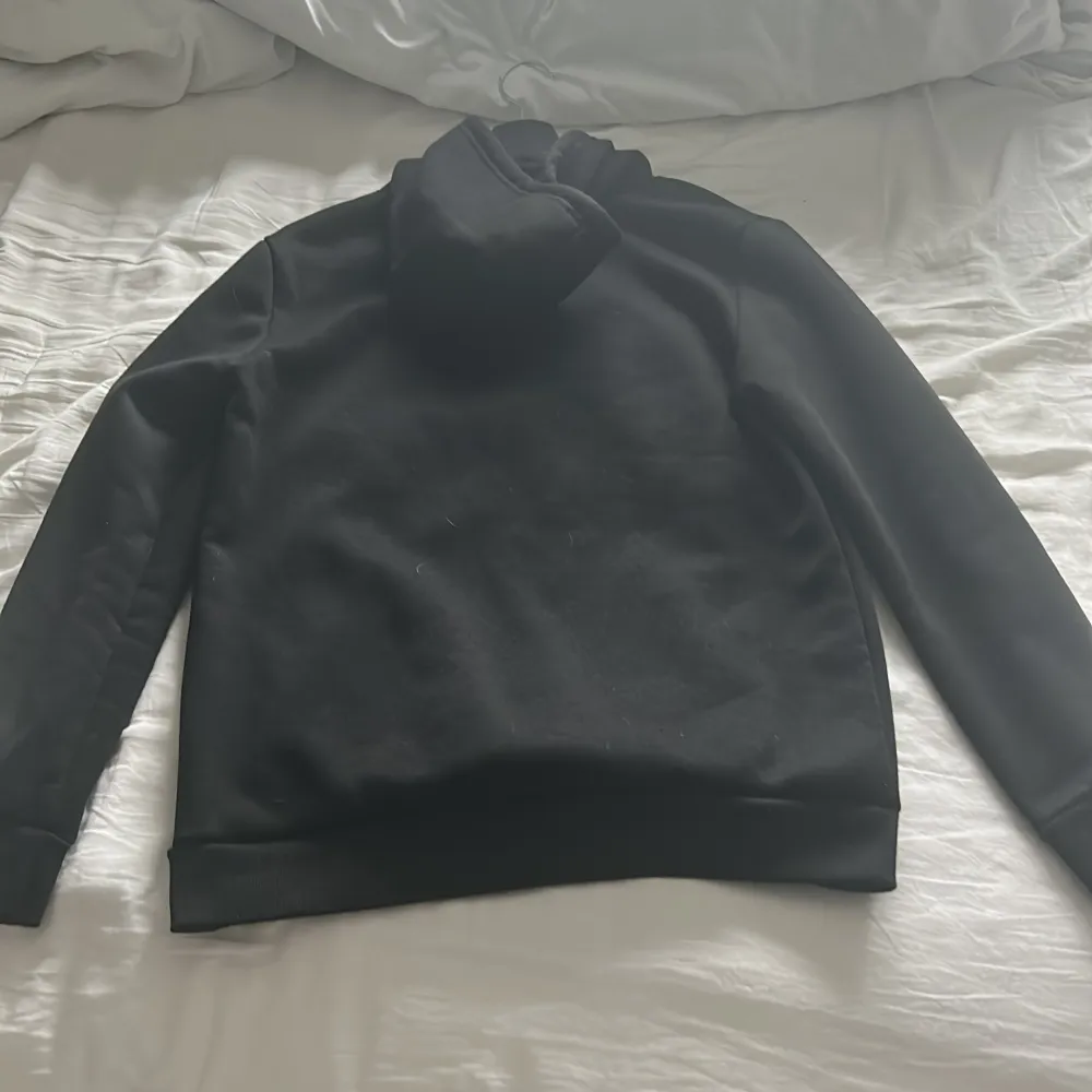 Säljer en stilren svart hoodie från Hugo med stor vit logga på framsidan. Tröjan har en klassisk känguruficka och justerbar huva med dragsko. Perfekt för en avslappnad look.. Neuletakit & Villapaidat.