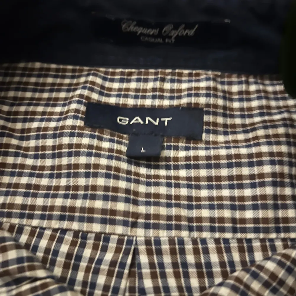 EliteVolt. Snygg rutig skjorta från GANT i brunt, blått och vitt. Skjortan har långa ärmar och knappar framtill samt på ärmsluten. Perfekt för en stilren look med broderad logga på bröstfickan.. Paidat.