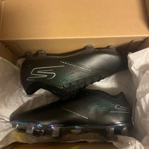 Fotsbollskor från skechers  - Orginal pris: 2500kr. OBS! Läs produkt beskrivningarna. Storlek 41. Sonen använde dessa fotbollsskor en träning och sedan märkte att dem tyvärr inte passade honom nu skulle vi gärna vilja sälja dem. Ingår med en påse för fotbollsskorna och även boxen.  Ovandel i premiumsyntet som lätt glider runt foten för en exceptionell passform, samtidigt som den ger ökad hållbarhet och oöverträffad bollkontroll. Skornas färger på botten är lite borta men glänser fortfarande, skosnöret är lite sönder.