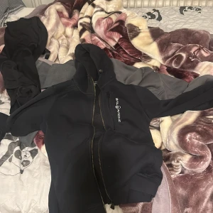 Svart hoodie från Sail Racing - Säljer en svart hoodie från Sail Racing med dragkedja och huva. Den har en broderad logotyp på bröstet och en annan detalj på ärmen. Perfekt för en casual look.