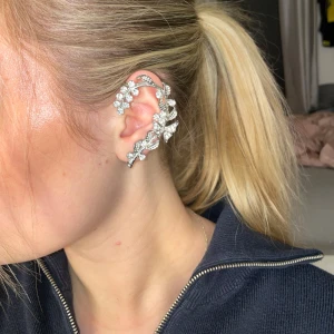 Silverfärgat öronsmycke med blommotiv - Jättefint öronsmycke i silver färg med bling stenar. Fästs fast med ett vanligt ”örhänge” längst ner som man fäster i sitt tagna hål📿 Använts 1-2 gånger och har steriliserats såklart!