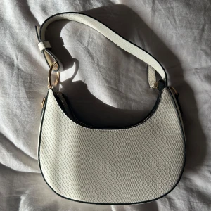 Vit handväska med gulddetaljer - Snygg vit handväska i nyskick med krokodilaktigt mönster och guldfärgade detaljer. Väskan kommer med en justerbar axelrem och säljs då den aldrig använts💕