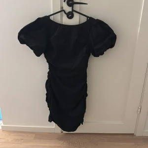 Svart kortklänning,  med puffärmar - Snygg svart kortklänning med puffiga kortärmar och rynkade detaljer. Klänningen ska sitta tight. Storlek 34, använd en gång 