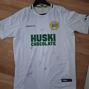Vit fotbollströja från Craft - Säljer en vit Hammarby if herrlag fotbollströja från Craft med gröna detaljer och tryck av 'Huski Chocolate' på framsidan. Tröjan är kortärmad och har flera autografer på framsidan. Perfekt för samlare eller fans! Priset kan alltid diskuteras!