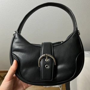 Handväska med spänne - Snygg svart handväska i skinn med ett stilrent spänne framtill från MANGO säljs inte längre