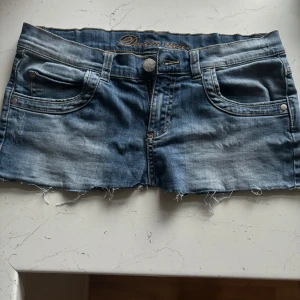 Lågmidjad Blå jeansshorts  - Snygg lågmidjad blå jeanskjol med slitna kanter. Perfekt för en avslappnad stil. As najs till sommaren.
