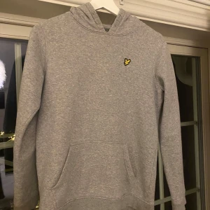 Grå hoodie från Lyle & Scott - Säljer en stilren grå hoodie från Lyle & Scott Junior. Tröjan har en klassisk design med en liten broderad logotyp på bröstet och en bekväm huva. Perfekt för en avslappnad look.