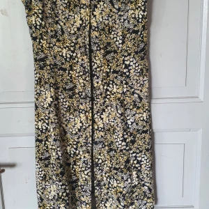 Blommig långklänning med knytning - Säljer en superfin klänning med blommigt mönster i svart, vitt och gult. Klänningen har en v-ringad hals och en knytning i midjan som ger en fin passform. Perfekt för sommarens alla fester och tillfällen! 🌸