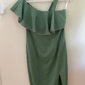 Festklänning - En fin och vacker asymmetrisk midifestklänning i en fin ljusgrön färg i storlek M. Speciell design med volanger. Använd endast en gång och är som nyskick. Det är möjligt att mötas upp. 