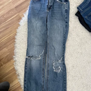 Blå jeans med slitningar - Säljer ett par blå jeans med coola slitningar på benen. De är i en straight fit och har en normal midja. Perfekta för en avslappnad och trendig look. Passar bra till både vardag och fest!