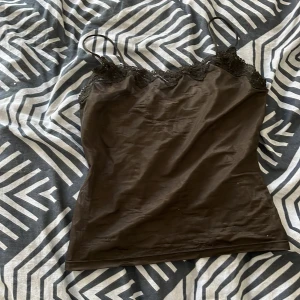 Svart linne med spetsdetaljer - Säljer ett svart linne med smala axelband och fina spetsdetaljer längs halsringningen. Perfekt för både vardag och fest! 🖤