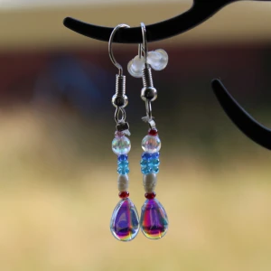 Färgglada örhängen med pärlor - Säljer ett par superfina örhängen med färgglada pärlor. De har en mix av blå, röda och genomskinliga pärlor som ger en härlig regnbågseffekt. Perfekta för att liva upp vilken outfit som helst! 💙