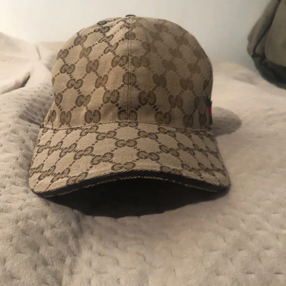 Säljer en snygg beige keps från Gucci med deras ikoniska GG-mönster. Kepsen är i storlek XS (56 cm) och har en justerbar rem baktill för perfekt passform. Perfekt accessoar för att lyfta din outfit!. Accessoarer.