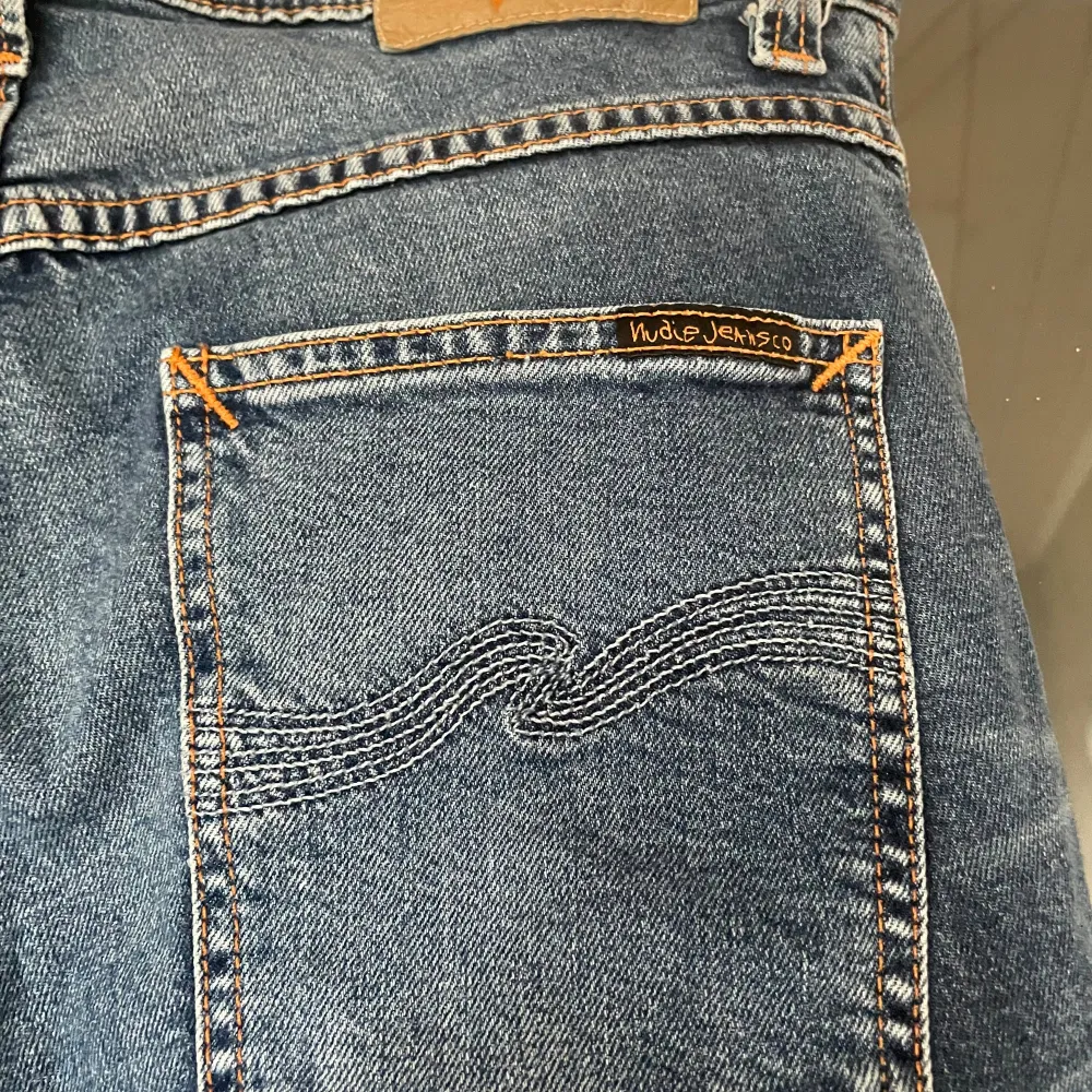 Säljer ett par snygga blå jeans från Nudie Jeans i modellen Grim Tim. De är i storlek W30 L32 och är tillverkade av 98% ekologisk bomull och 2% elastan, vilket gör dem både bekväma och stretchiga. Perfekta för vardagsbruk!. Jeans & Byxor.