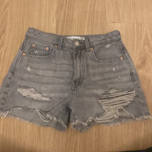 Grå jeansshorts från Stradivarius - Säljer ett par grå jeansshorts från Stradivarius i storlek 36. De är i vintage-stil med slitna detaljer och fransiga kanter. Perfekta för en avslappnad sommarlook! köpta i Spanien. pris kan som vanligt diskuteras❤️