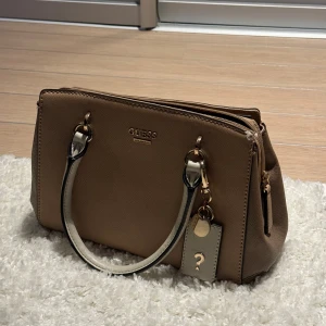 Jättesöt liten guess väska - Jättesöt guess väska i liten/mellan storlek. Köptes i New York för några år sedan man knappt använd. Perfekt skick på utsidan men lite märken på insidan💕 Perfekt present till lilla syster, kusin eller någon annan yngre tjej!