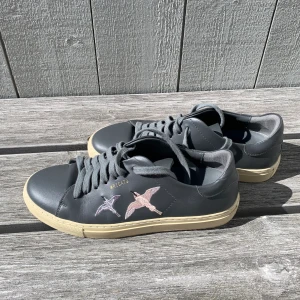 Axel Arigato sneakers - Sneakers från Axel Arigato, B Bird. Gjorde i grå läder med en ljusrosa och en ljuslila fågel på sidan av varje sko. Mycket sparsamt använda och de är så gott som nya. Nypris cirka 2200kr.