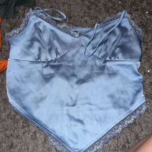 Ljusblå satinlinne från Bik Bok - Säljer ett superfint ljusblått linne från Bik Bok i storlek M. Det är gjort av satin och har spetsdetaljer längs kanterna. Perfekt för sommaren eller en festkväll! 💙