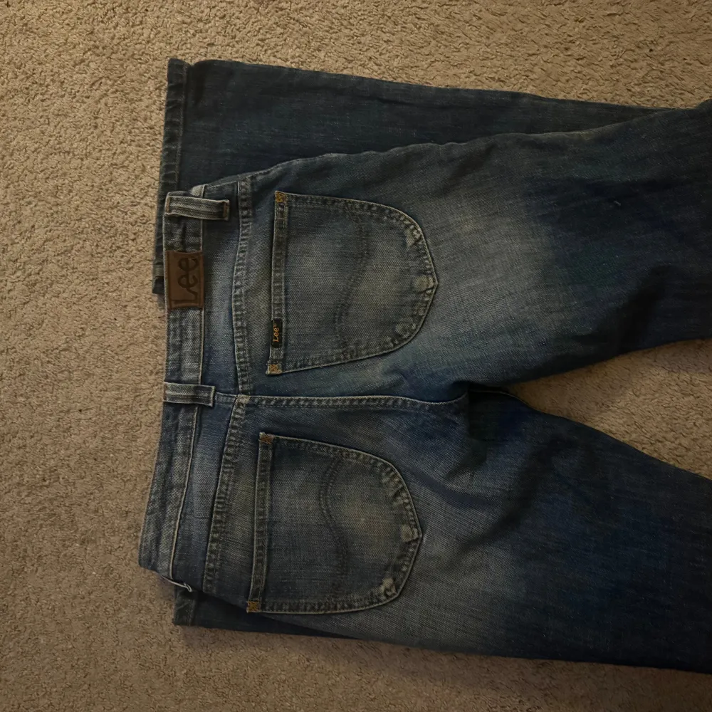 Säljer ett par snygga blå jeans från Lee i storlek S. De är lågmidjade och har en straight passform. Jeansen är i bra skick förutom en liten fläck på knät från en penna, inte testat att ta bort . Jeans & Byxor.