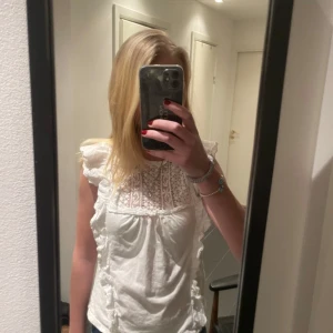 Vit blus från Mangl - Säljer en söt vit blus från Mango med spetsdetaljer och volanger. Blusen är ärmlös och har en romantisk design som passar perfekt för vår och sommar. Perfekt för att ge en feminin touch till din outfit.