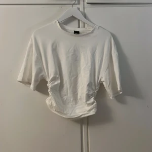 Offwhite t-shirt med rynkdetalj från Gina Tricot - Säljer en mjuk offwhite t-shirt från Gina Tricot med rynkdetalj i midjan. T-shirten har en rund halsringning. Perfekt för en stilren och bekväm look. Nypris: 259,95kr