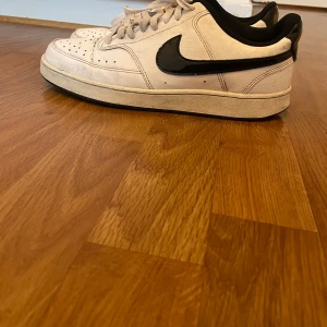 Vita och svarta Nike sneakers - Snygga vita sneakers från Nike med svart swoosh och detaljer. Skorna är i väldigt bra skick inte använda så mycket men lite smutsigt bara så måste ba torka de lite. 
