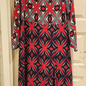 Mönstrad klänning från Closet London - Snygg klänning från Closet London med ett färgstarkt geometriskt mönster i rött, grått och svart. Klänningen har långa ärmar och en normal passform, perfekt för att sticka ut i mängden. Tillverkad i ett mjukt och bekvämt material.