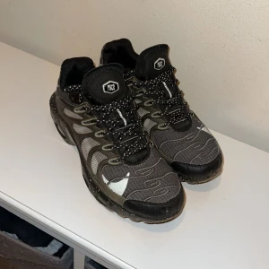 Svarta sneakers från Nike - Snygga svarta/olivgröna sneaker från Nike med ett unikt mönster och snörning. Skorna har en sportig design med detaljer i grått och vitt. Perfekta för en casual look.