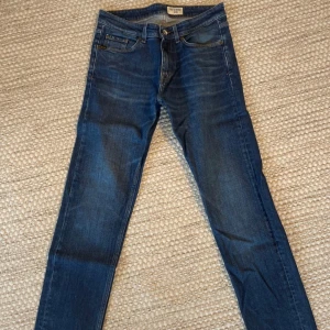 Blå jeans från Tiger of Sweden - Snygga blå jeans från Tiger of Sweden med klassisk femficksdesign och knappgylf. De har en stilren look med en läderpatch baktill. Perfekta för en stilren vardagslook. W30 L32.