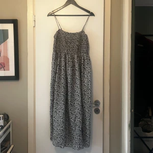 Blommig långklänning från & Other Stories - Säljer en vacker långklänning från & Other Stories med ett blommigt mönster i blått och vitt. Klänningen har smala axelband och en smockad överdel som ger en bekväm passform. Perfekt för varma dagar och somriga tillfällen. 🌸