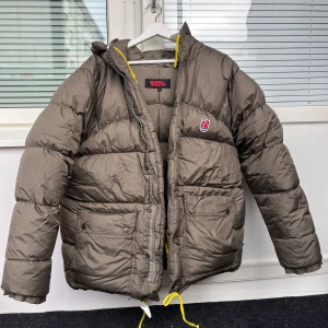 Fjällräven Expedition Jacka - Säljer en mörkgrön dunjacka från Fjällräven i storlek XS. Jackan har en pufferdesign med långa ärmar och fickor framtill. Jag vet inte om det är herr eller dammodellen, men är stor i storleken😇💓Dett är den varmare modellen som kostar 10.000kr nypris😇I RIKTIGT fint skick💓Lite märken av användning såsom mindre synliga fläckar!💓Och en lagning på vänster arm, se bild!Fråga jättegärna om du undrar något!😇