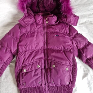 Lila dunjacka från MHM Fashion - Säljer en ursnygg lila dunjacka från MHM Fashion med fluffig fuskpäls på huvan. Jackan stängs med dragkedja framtill och har två stora fickor med knappar, samt flera fina utsmyckningar för en riktigt lyxig känsla! Insidan är fodrad med mjukt material för extra värme. Storlek 164 men passar mig som har S. Fler bilder kan skickas vid intresse! ❤️