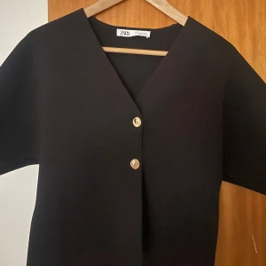Svart kofta från Zara - Snygg svart kofta från Zara med v-ringning och knappar framtill. Perfekt för en stilren look. Kortärmad design som passar bra till olika outfits.