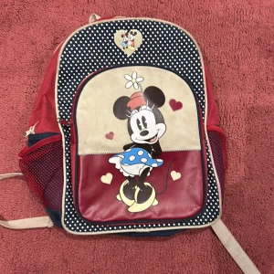 Mimmi Pigg ryggsäck - Charmig ryggsäck med Mimmi Pigg-motiv. Väskan har en röd och beige färgkombination med prickigt mönster och hjärtan. Perfekt för Disney-fans!