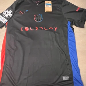 Svart fotbollströja från Nike - Snygg svart fotbollströja från Nike med röda och blå detaljer. Tröjan har korta ärmar och ett tryck på framsidan samt baksidan med nummer 19. Perfekt för fotbollsfans som vill ha en unik look på planen.