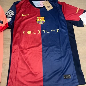 FC Barcelona fotbollströja - Snygg FC Barcelona tröja från Nike i rött och blått med klubbens emblem på bröstet. Tröjan har korta ärmar och ett unikt mönster med månfaser. På baksidan finns nummer 19 och texten 'Lamine Yamal'. Perfekt för fans som vill visa sitt stöd!