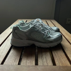 Silver och vita sneakers från New Balance 530 - Snygga och bekväma sneakers från New Balance i grått och vitt. Skorna har en klassisk design med snörning och en stabil sula. Perfekta för en avslappnad stil. OBS!!! Ingen innersula! Helt nya 