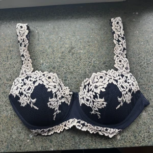 Mörkblå/marinblå bh med via spetsdetaljer från intimissimi - Fin intimissimi mörkblå bh med vackra vita spetsdetaljer. Bh:n har justerbara axelband och hakknäppning där bak. Som helt ny och knappt använd. Storlek 80 B