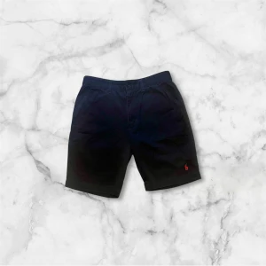 Marinblå shorts från Polo Ralph Lauren - Snygga marinblå shorts från Polo Ralph Lauren med röd broderad logga. Tillverkade i 100% bomull för en bekväm känsla. Perfekta för en avslappnad stil. Mycket bra skick