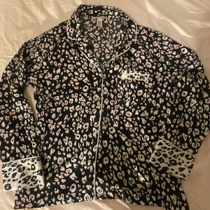Leopardmönstrad pyjamas skjorta från Victoria's Secret - Snygg leopardmönstrad pyjamas skjorta från Victoria's Secret i svart, rosa och vit. Skjortan har långa ärmar och knappar framtill. Perfekt för en trendig look med en touch av lyx. Säljer då den är för liten för mig! 