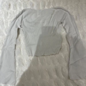 Vit ribbad långärmad topp - Säljer en stilren vit ribbad topp med långa ärmar. Toppen har en rundad u-ringning på ryggen och är perfekt för lager-på-lager eller att bära som den är. Enkel och mångsidig i garderoben.