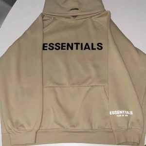 Beige hoodie Essentials Fear of God - Säljer en snygg beige hoodie från Essentials Fear of God. Den har en klassisk design med svart text på framsidan och en praktisk känguruficka. Perfekt för en stilren och avslappnad stil. Fler frågor, kom dm.