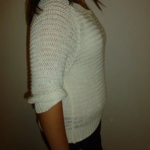 Vit stickad trekvart tröja - Här kommer en vit stickad tröja med trekvartsärmar. Tröjan har en luftig och bekväm passform. Den är enkel och stilren, vilket gör den lätt att matcha med olika outfits.